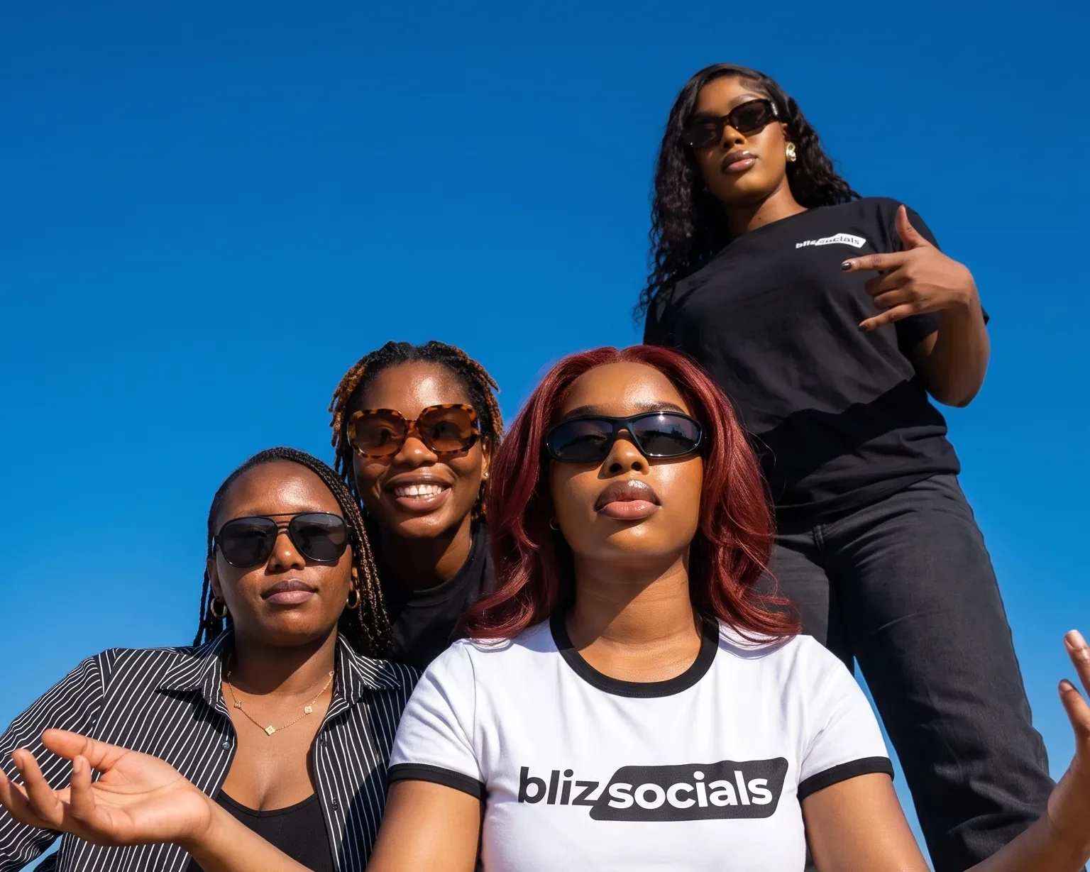 Four members of the Blizsocials team outdoors in branded shirts against a clear blue sky